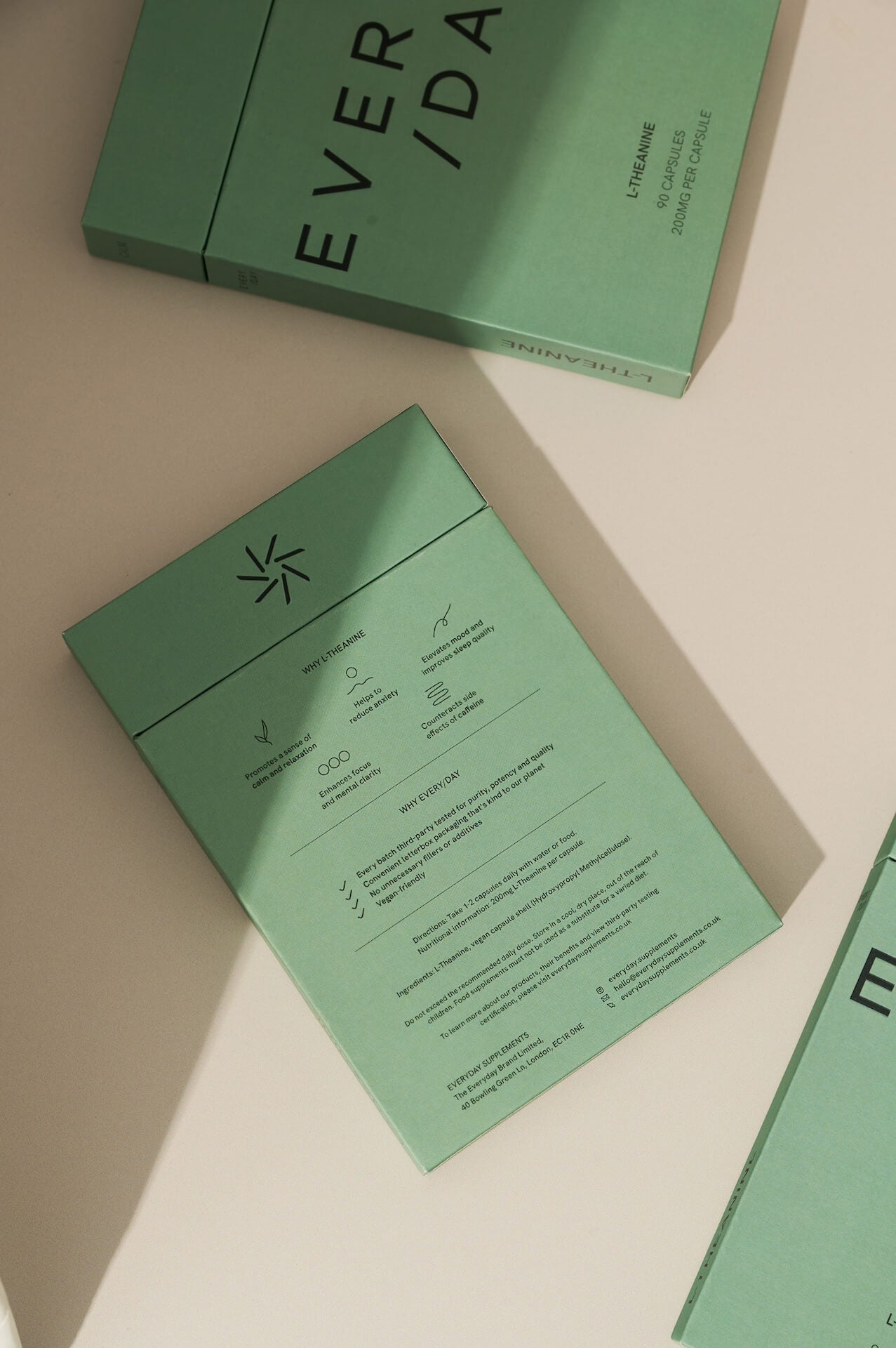 Flat lay of three Everyday Supplements boxes in sage green, with one positioned to show the back label listing ingredients, dosage and usage, highlighting the brand’s commitment to clarity and quality.