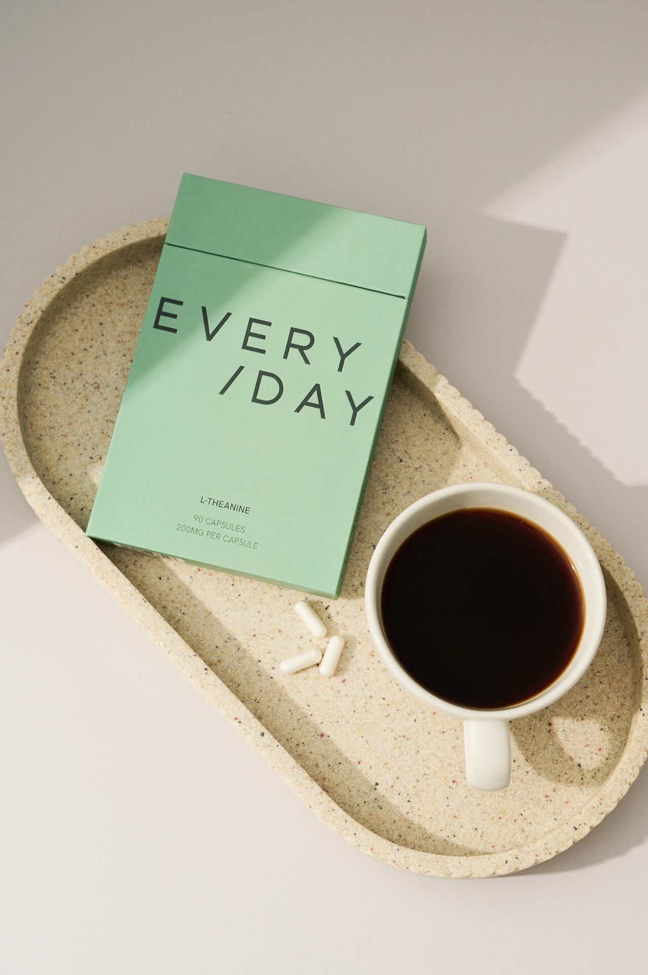 Lifestyle product photo featuring Everyday Supplements sage green packaging alongside a cup of coffee and L-Theanine capsules arranged neatly on a tray, a calm morning ritual captured in a minimal, modern setting.